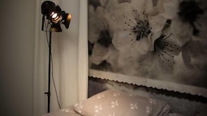 Une chambre à coucher avec un lit, une lampe sur pied et un mur décoré d’œuvres d’art florales.