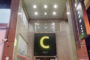 A hotel entrance with a prominent illuminated 'C' sign, a glass facade, and a ceiling with recessed lighting.