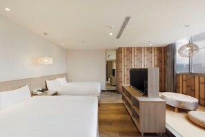 A modern hotel room with two beds, a TV, and a seating area.