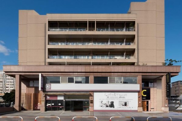 A multi-story building with a central entrance, balconies on each floor, and a storefront with a sign.