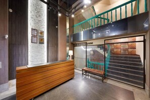 Un área de recepción con un banco de madera, una pared con cuadros enmarcados y una escalera con barandas verde azulado.