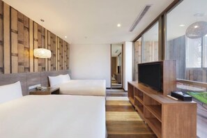 A hotel room with two beds, a TV, wooden panel wall, and a large window.