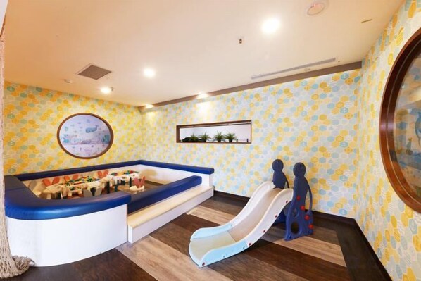 Zona infantil con tobogán, asientos y una pared decorada con un motivo circular.