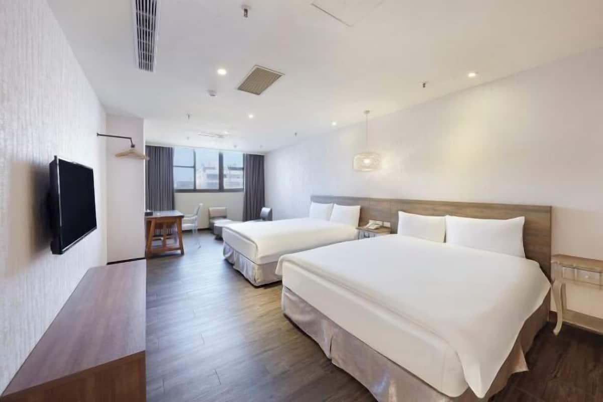 Une chambre d’hôtel avec deux lits, un bureau, une chaise, une télévision et une fenêtre.