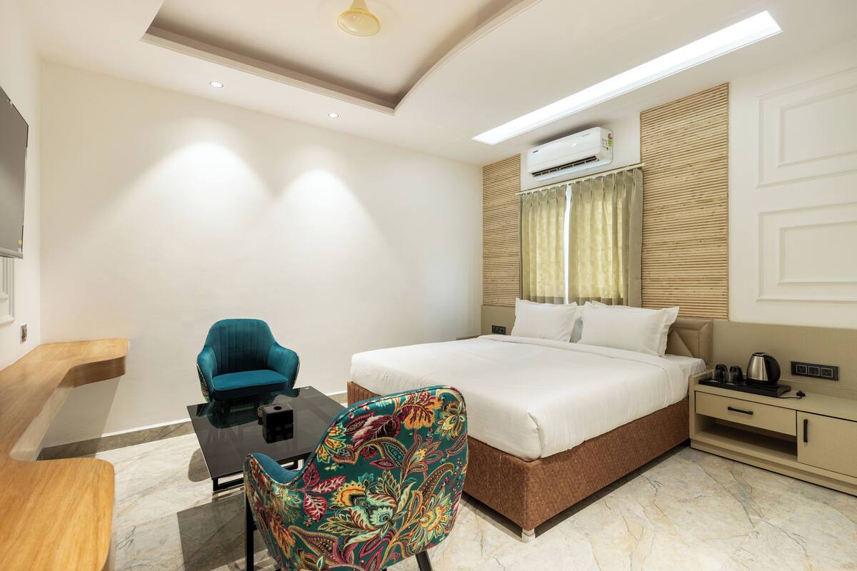 A modern hotel room with a large bed, a desk, a chair, and an air conditioning unit.