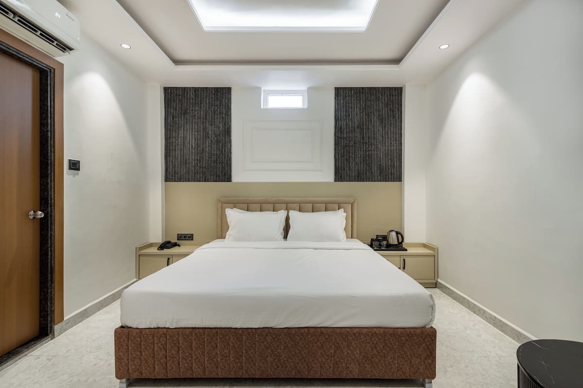 A hotel room with a large bed, a bedside table with a phone and a lamp, a small window, and a ceiling light.