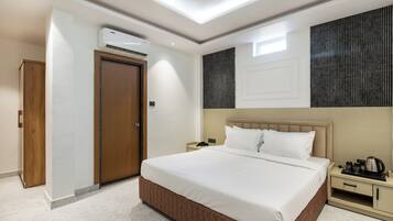 A hotel room with a large bed, a bedside table with a phone and a kettle, a wardrobe, and an air conditioning unit.