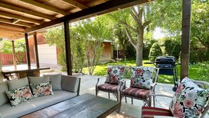 An outdoor patio with a wooden ceiling, a sofa set with floral cushions, a wooden table, and a grill. - Newly Renovated 4 bedroom home (West Valley City)