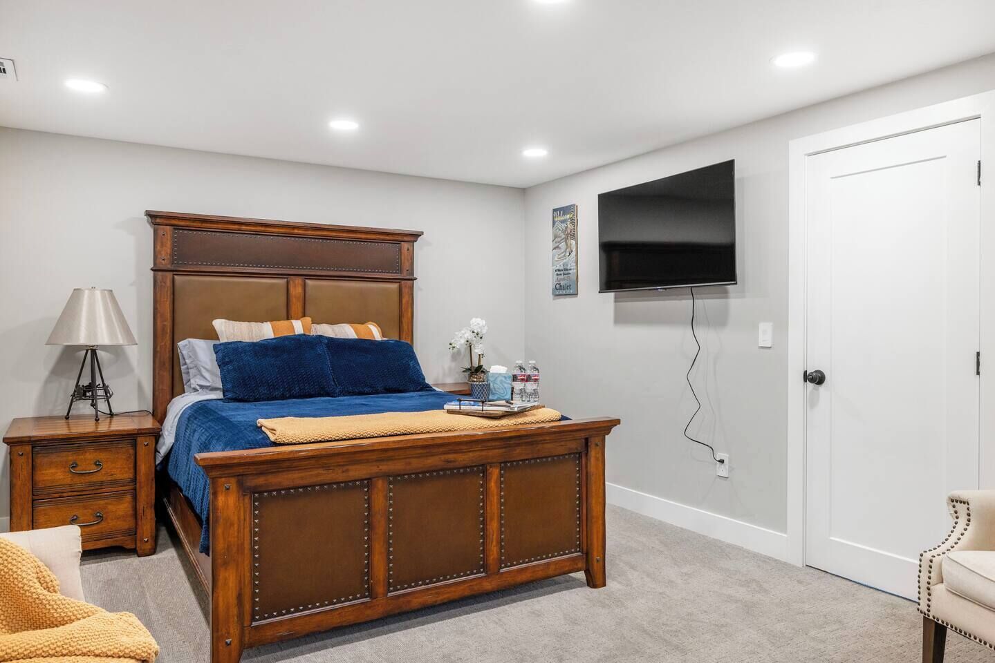 Une chambre à coucher avec un lit en bois, une table de chevet avec une lampe, un téléviseur fixé au mur et une porte.