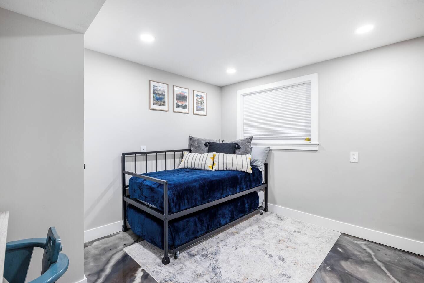 A bedroom with a bunk bed, a window with blinds, and three framed pictures on the wall.