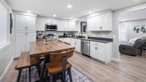 A modern kitchen with white cabinets, a wooden dining table, and a gray sofa in the living area. - Newly Renovated 4 bedroom home (West Valley City)