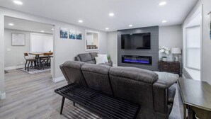 A modern living room with a grey sectional sofa, a flat-screen TV mounted on the wall, and a dining area with a wooden table and chairs. - Newly Renovated 4 bedroom home (West Valley City)