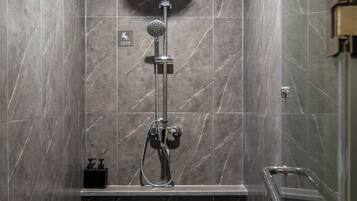 A shower area with a handheld showerhead, a wall-mounted control panel, and a small shelf with toiletries.