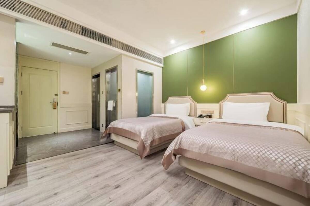 A hotel room with two beds, a green accent wall, and a modern design.