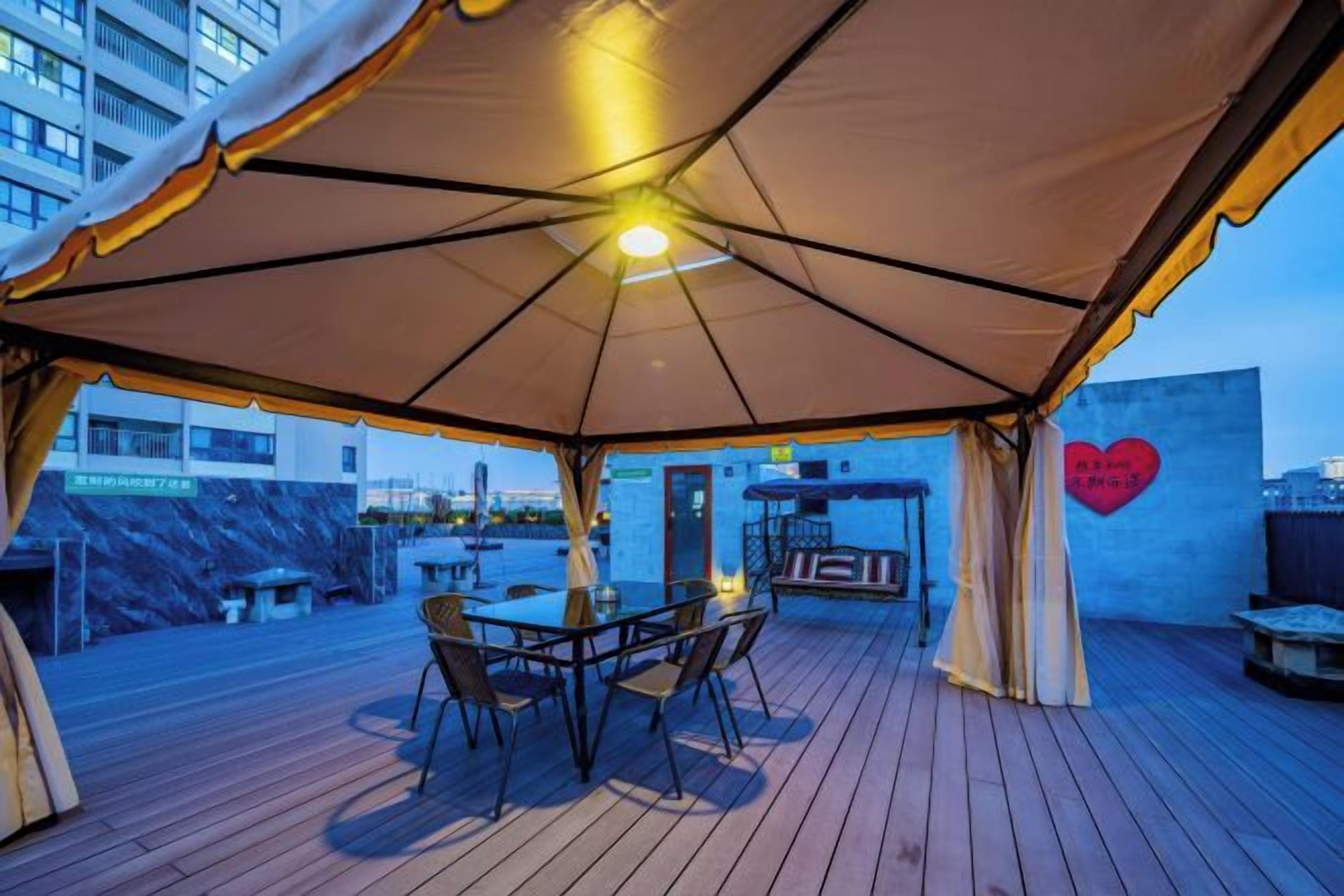 An outdoor patio with a table and chairs under a large umbrella, a barbecue grill, and a heart-shaped decoration on the wall.