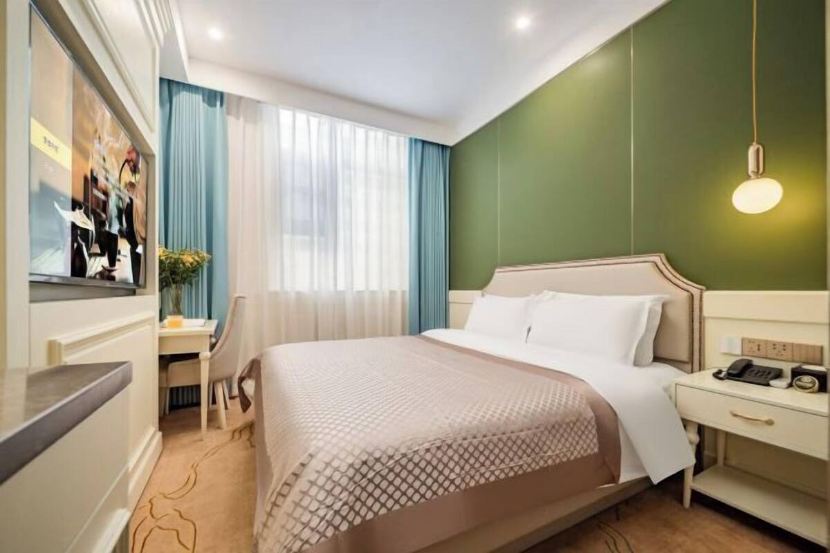 A hotel room with a bed, bedside table, desk, and chair.
