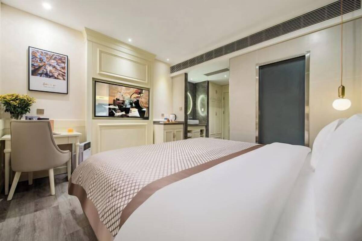 A hotel room with a large bed, a desk, a chair, a television, and a door.