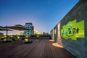 An outdoor seating area with tables and umbrellas, a city skyline in the background, and a wall with illuminated signage. - Xi'an Sende Hotel (Chang'an University Wenyi Road Metro Station Branch), (Xi'an)