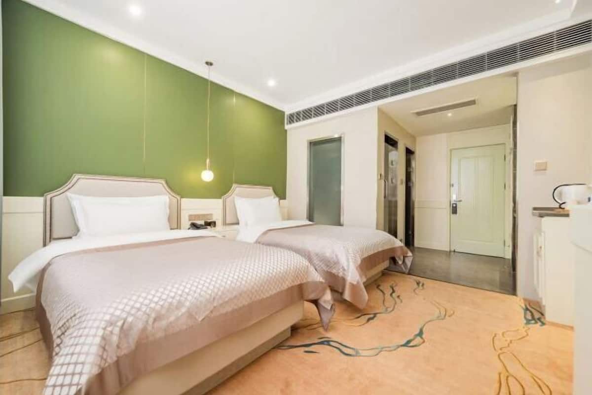 A hotel room with two beds, a green accent wall, a patterned carpet, and a modern design.