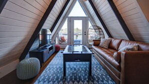 A cozy attic room with a brown leather sofa, a glass-top coffee table, and a ceiling fan.