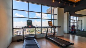 A gym with treadmills and a weightlifting area, large windows with a city view.