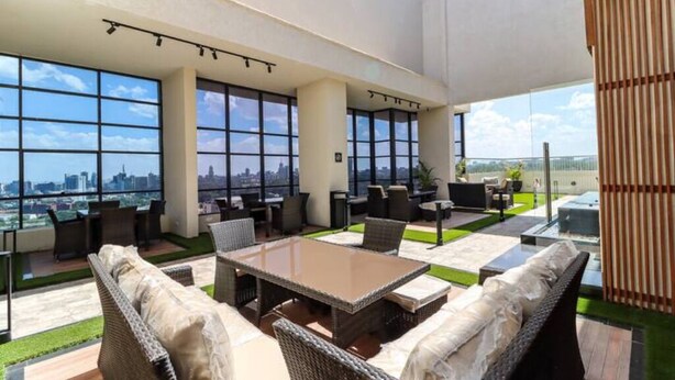 A spacious outdoor lounge area with a city view, furnished with wicker sofas and tables, and a wooden privacy screen.