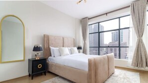 A bedroom with a large bed, a nightstand, a mirror, and a window with curtains.