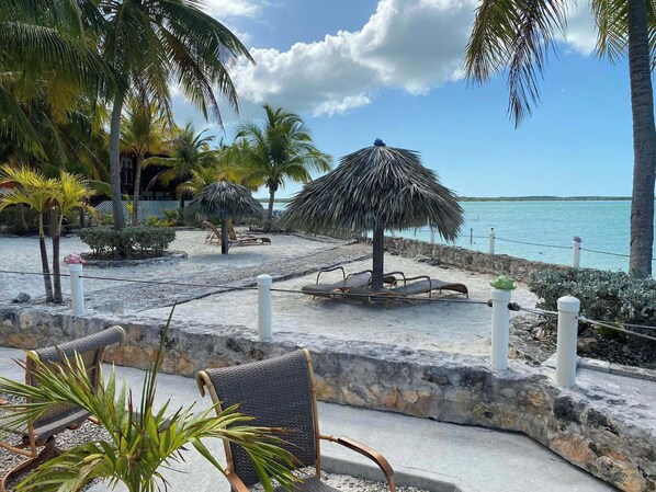 A beachside lounge area with lounge chairs, a thatched umbrella, and palm trees.