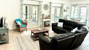Un salon spacieux avec un canapé en cuir noir, un fauteuil en osier, une table basse et un coin repas comprenant des chaises et une table.