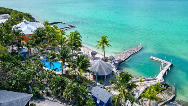 Un complexe hôtelier tropical doté d’une piscine, de palmiers et d  ’une jetée s’avançant dans des eaux turquoise.