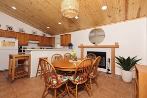 A wooden-paneled kitchen with a dining table and chairs, a hanging light fixture, and a potted plant.