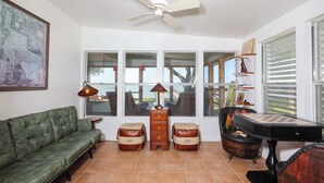 A living room with a green sofa, a wooden chest of drawers, a table, and a ceiling fan.