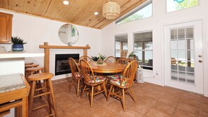 A dining area with a wooden table and chairs, a hanging light fixture, and a fireplace.