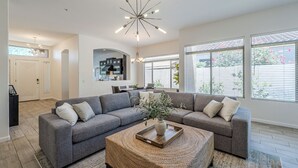A spacious living room with a grey sectional sofa, a round coffee table with a tray, and a modern chandelier. - Greyhawk - Pool - Chef's Kitchen - Golfer's Dream Location (Scottsdale)