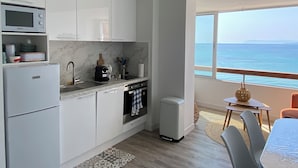 A modern kitchen with white cabinets, a microwave, a coffee maker, and a view of the sea through a large window. - Waterfront studio with enchanting views (Six-Fours-les-Plages)