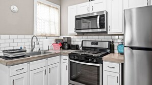 Een moderne keuken met witte kasten, roestvrijstalen apparatuur, een magnetron, fornuis en een koelkast.