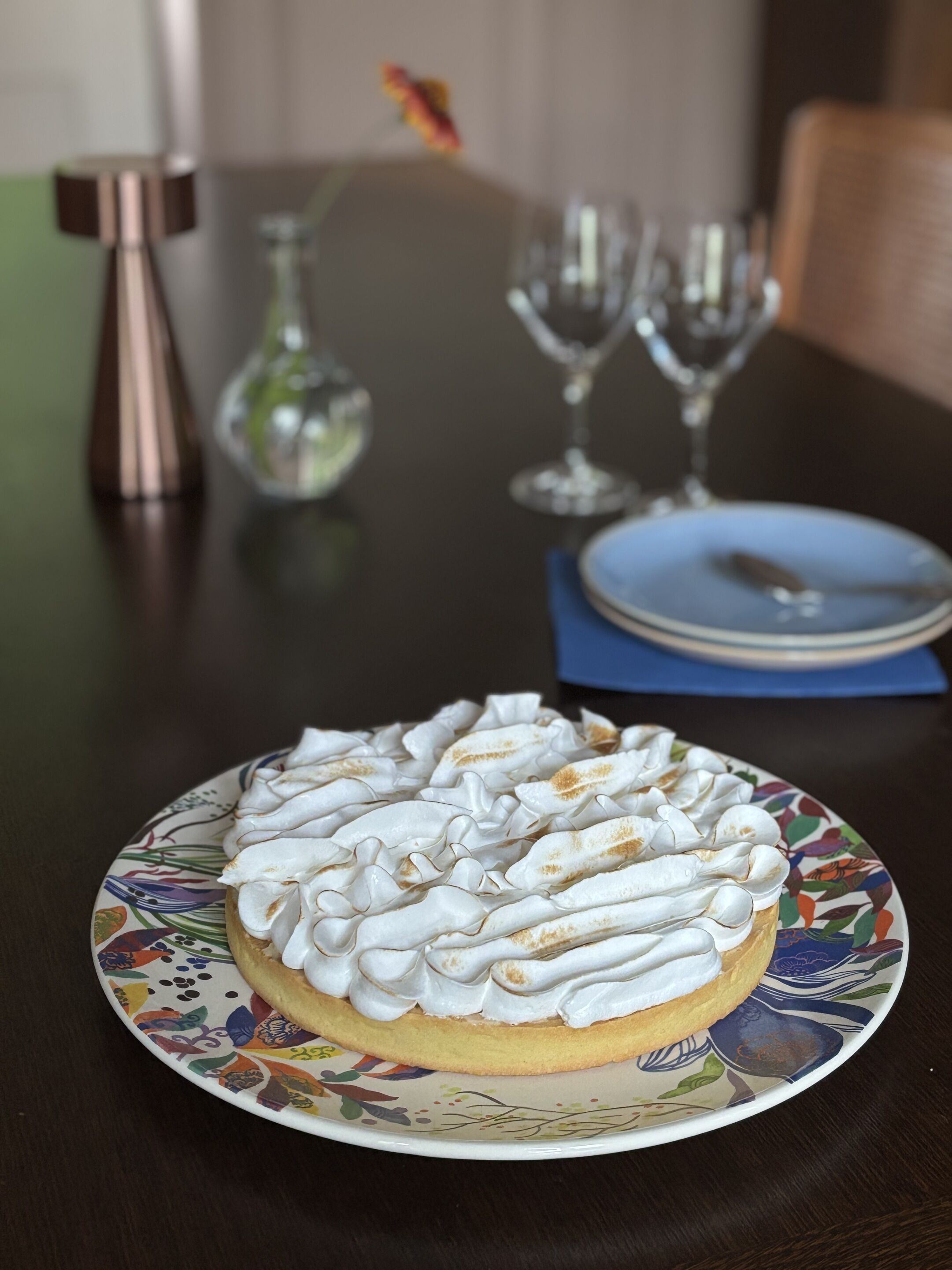 Un postre en un plato con diseño floral, una mesa con un jarrón y una silla.