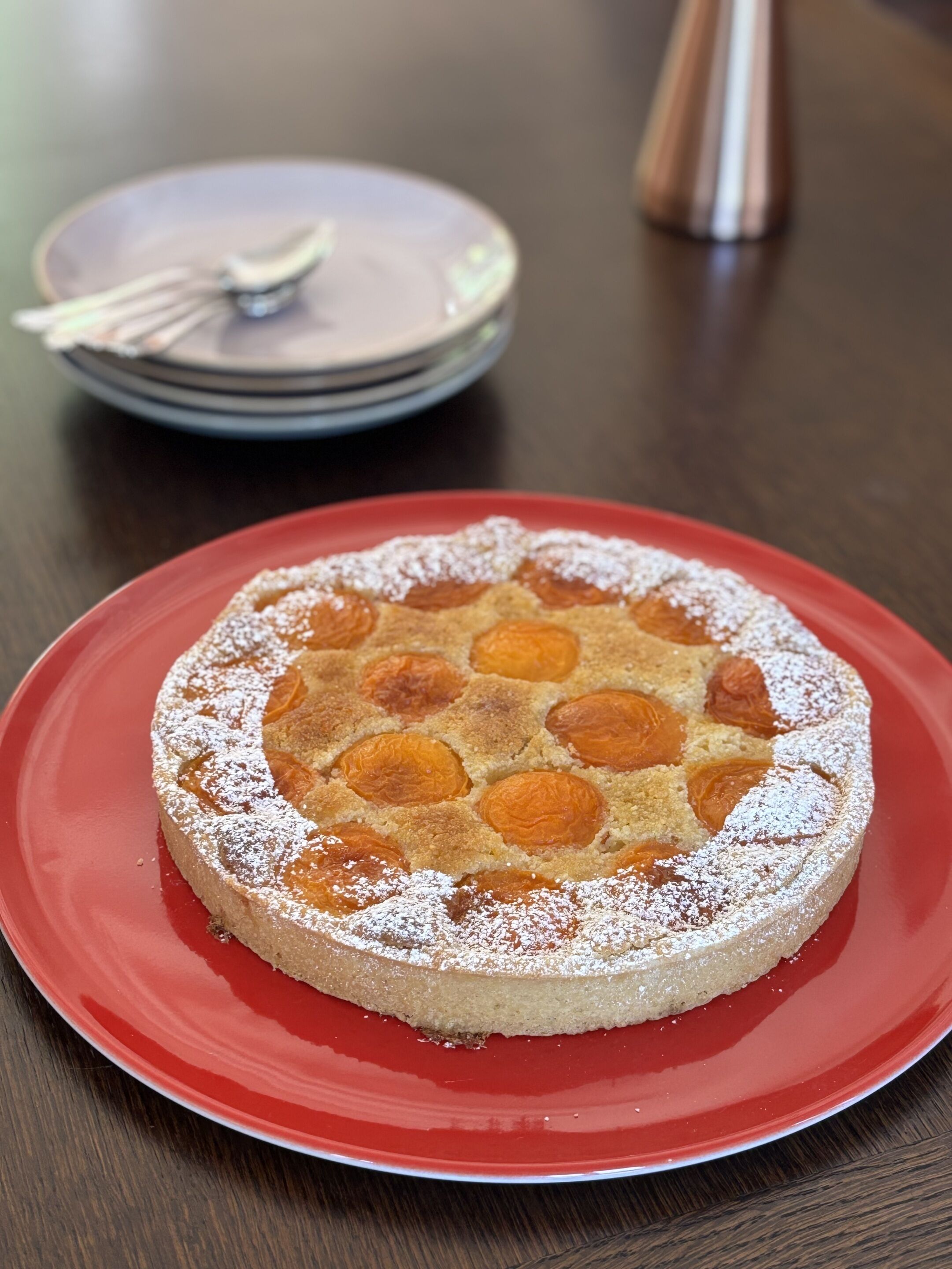 Un gâteau rond, garni d’abricots, présenté sur une assiette rouge.
