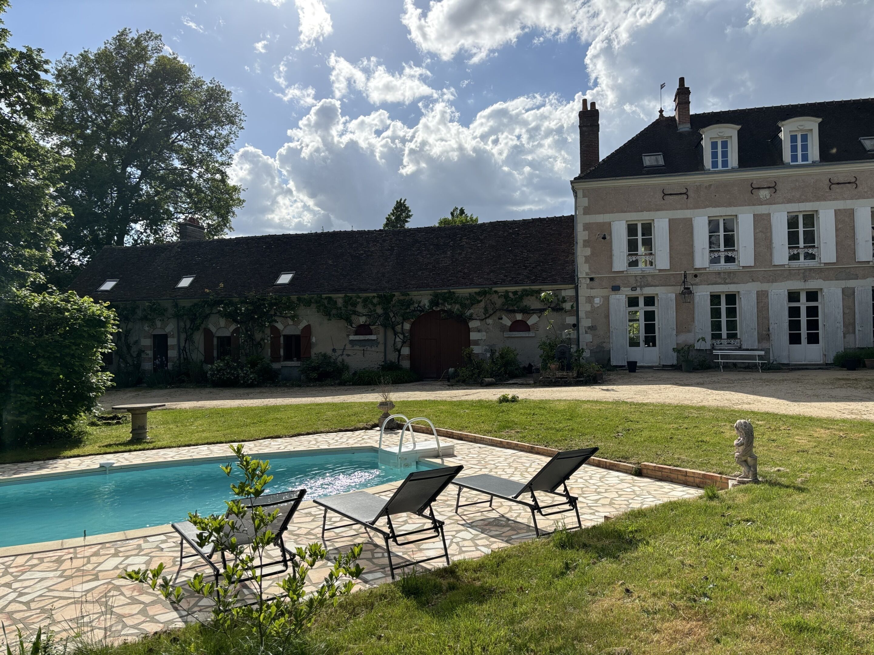 A swimming pool with lounge chairs, a stone patio, and a large building with a tiled roof and multiple windows.
