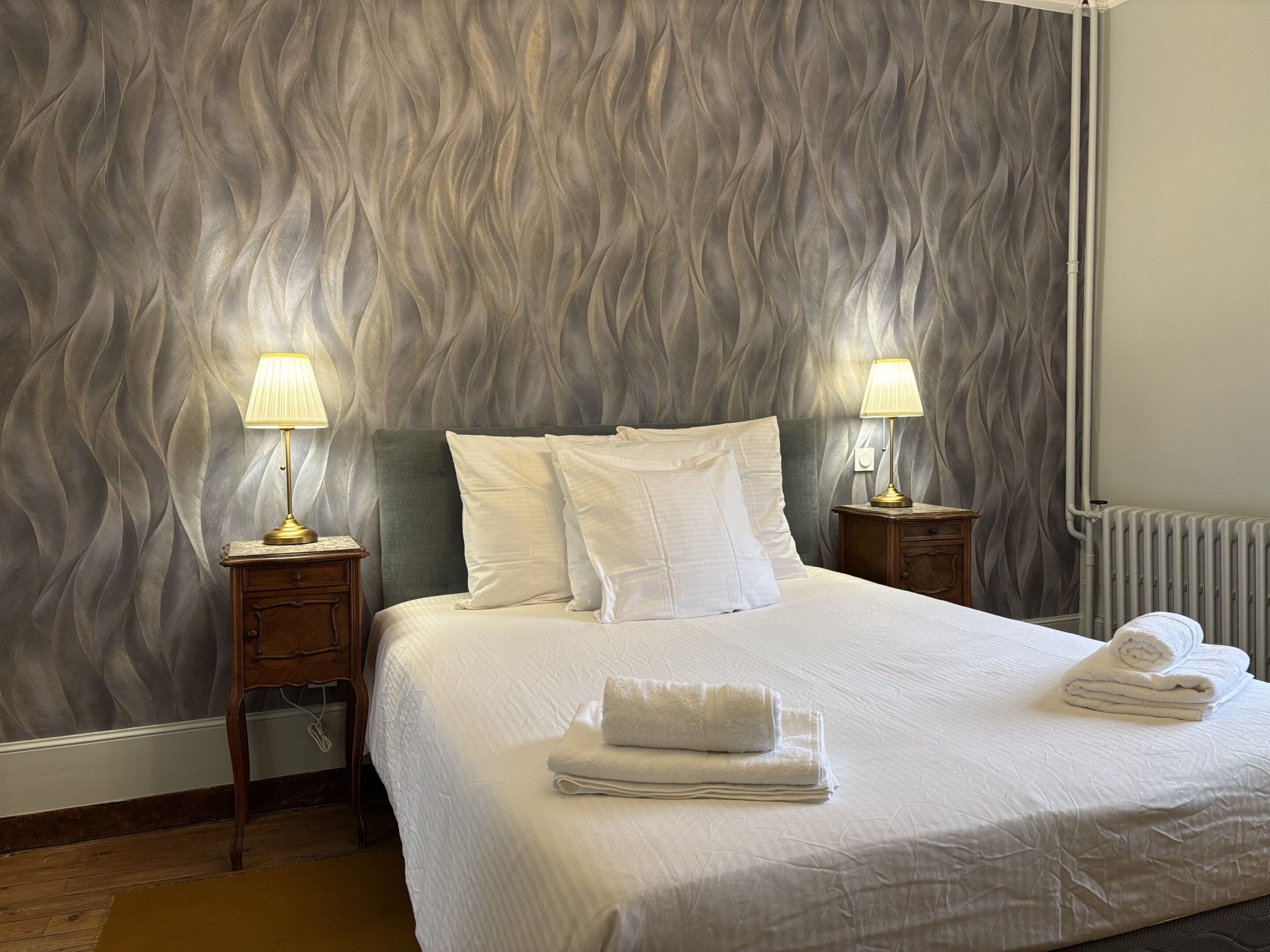 A neatly made bed with white linens, two bedside lamps, and a folded towel on the bed.