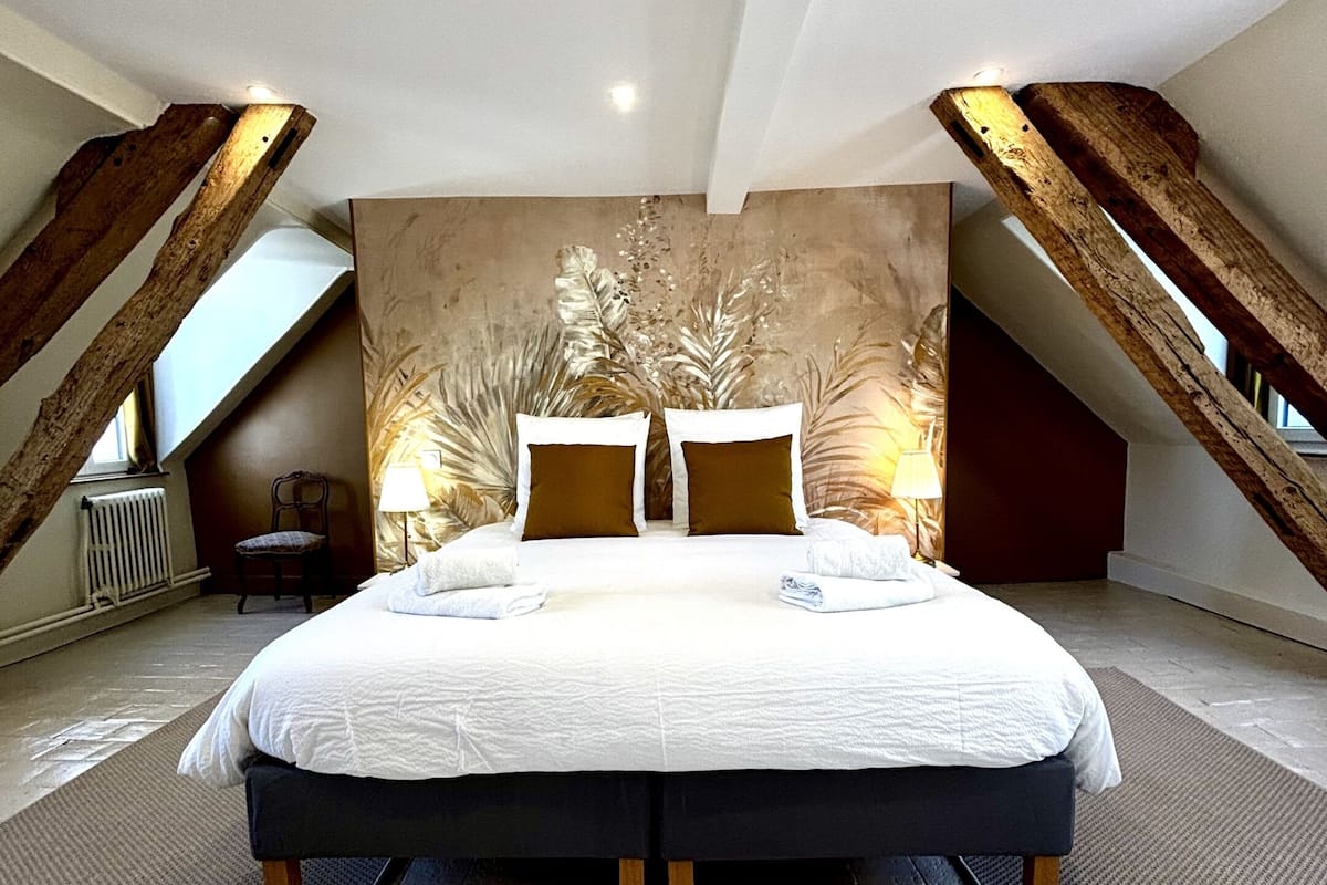 Un dormitorio amplio con una cama grande, un muro decorativo y un techo inclinado.