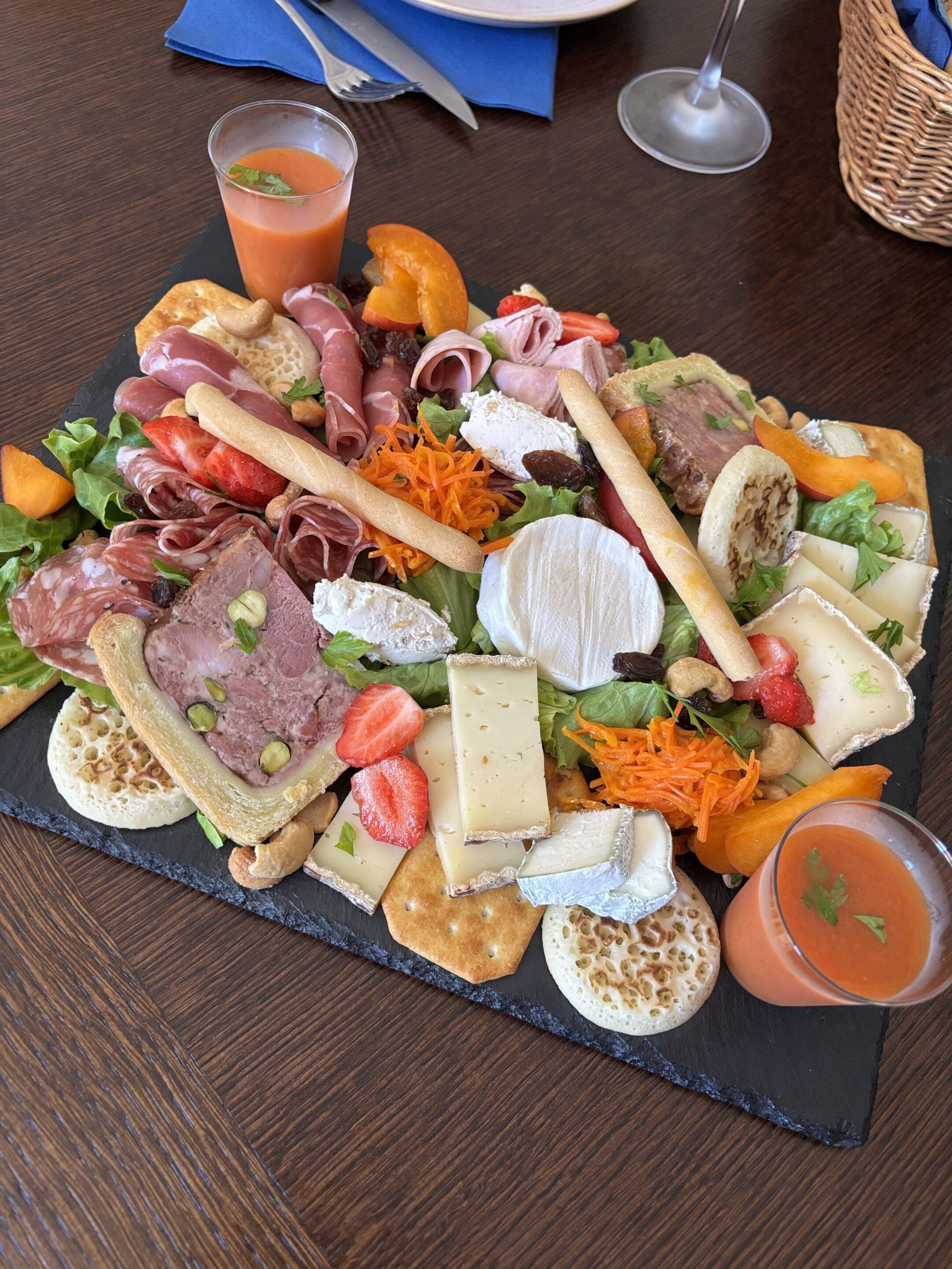 A charcuterie board with various cheeses, meats, fruits, and vegetables on a slate board.