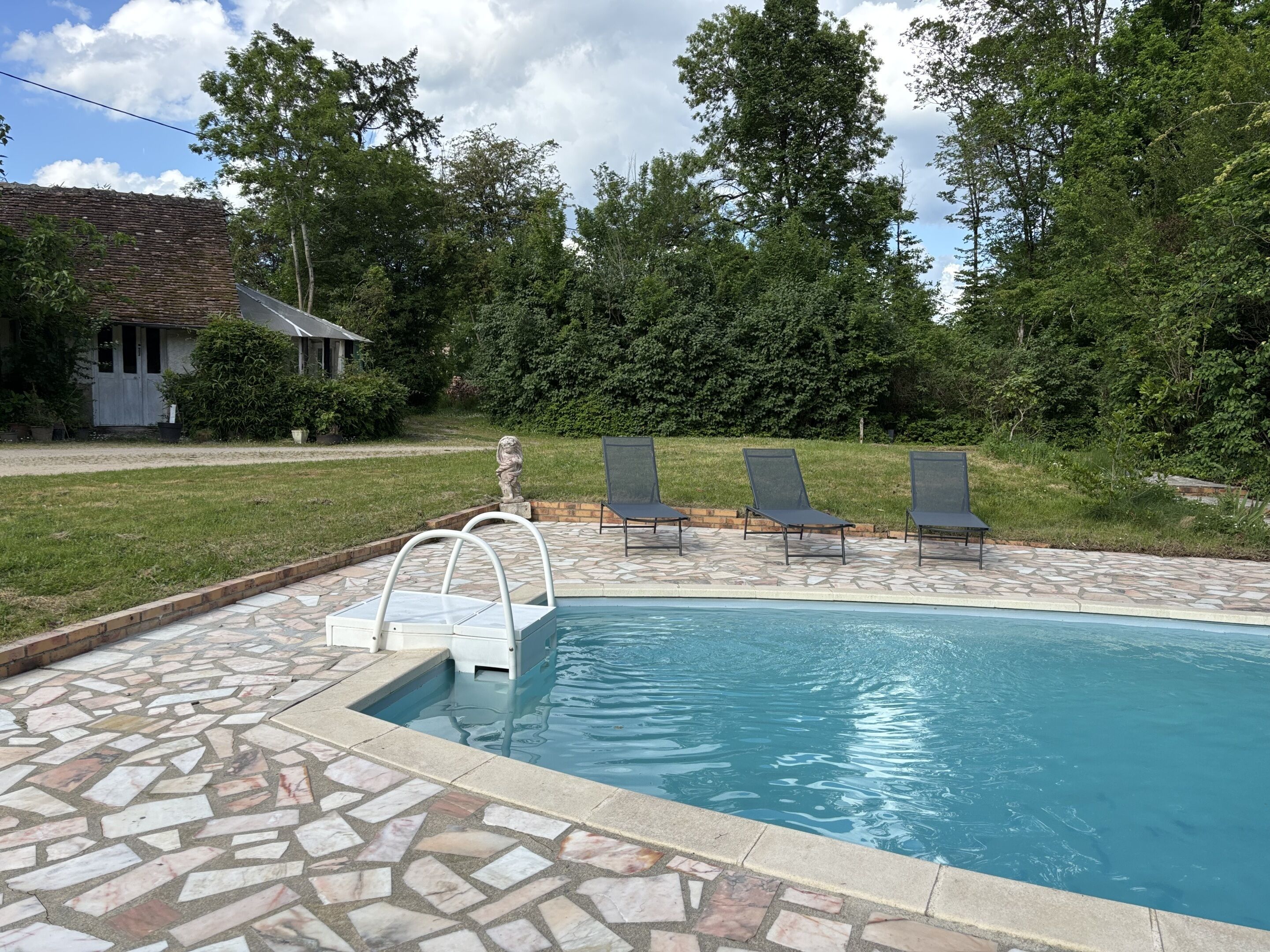A swimming pool with a stone deck, three lounge chairs, and a statue.