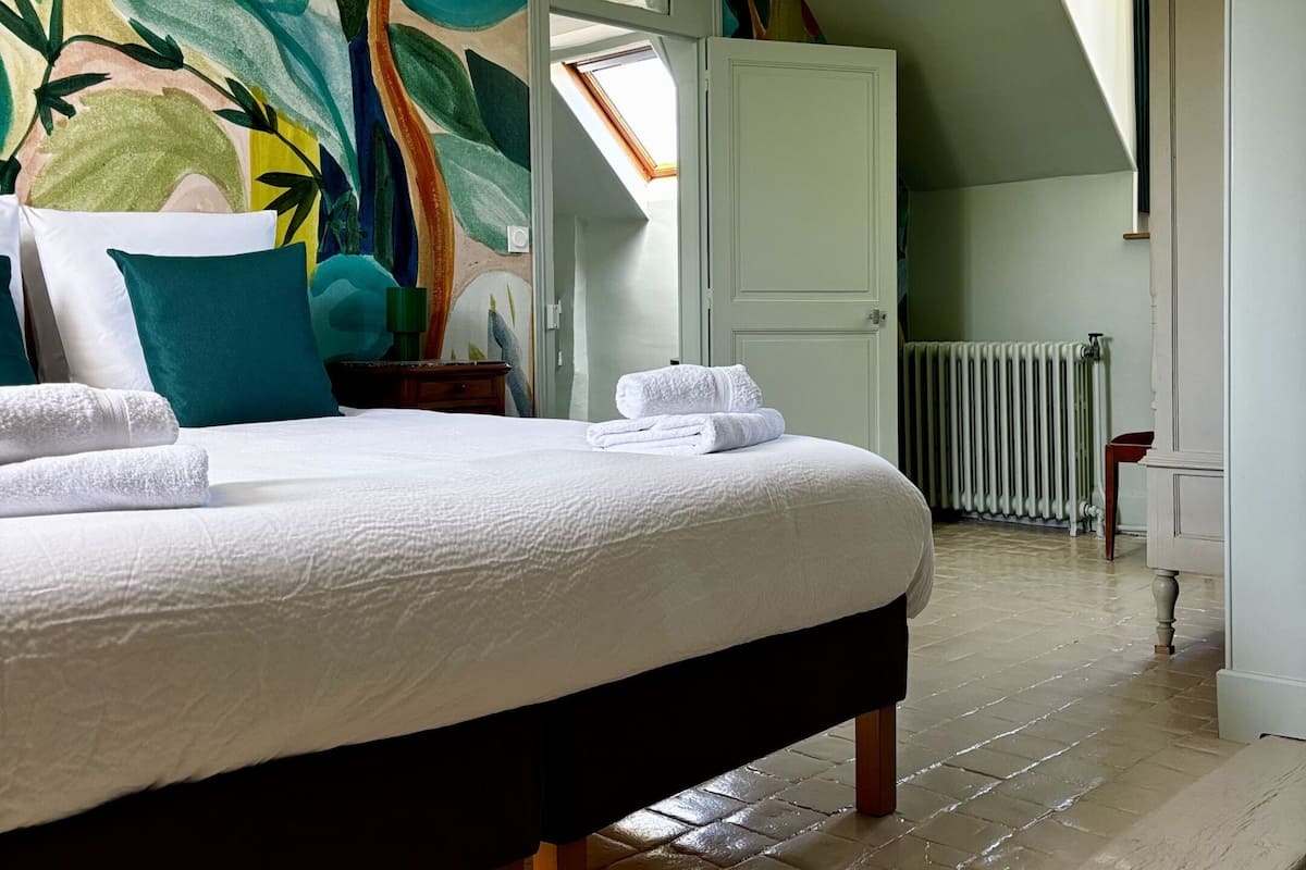 Un dormitorio con cama, un mural colorido, un tragaluz y vista a un pasillo.