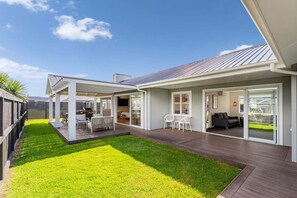 Ein modernes Haus mit überdachter Terrasse, Rasenfläche und Essbereich.