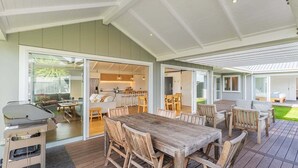 An outdoor dining area with a wooden table and chairs, a grill, and a view of the interior through glass doors.