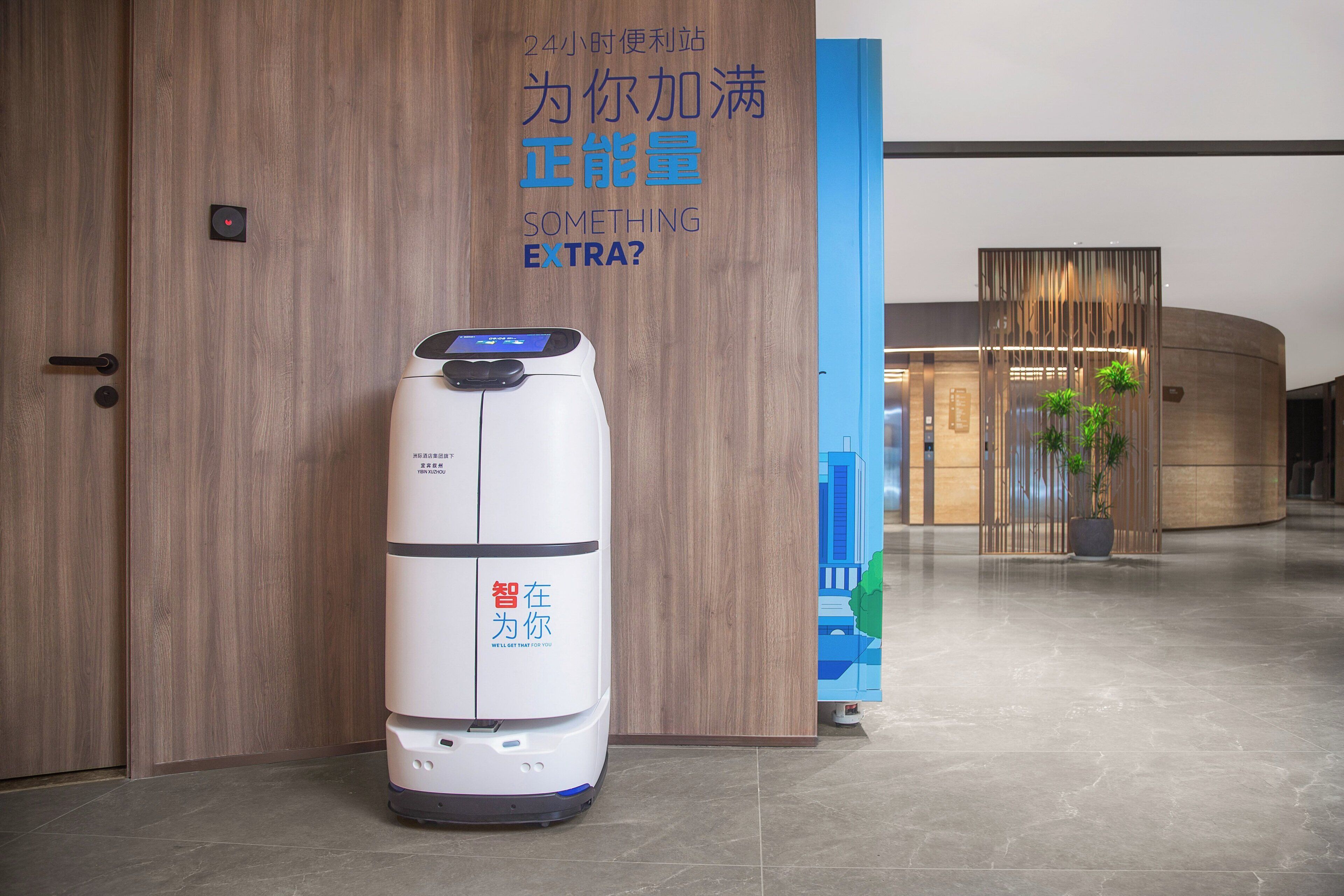 A robot vacuum cleaner in a modern lobby with wooden walls and a blue accent wall.
