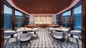 Un comedor moderno con piso de diseño geométrico, una zona de bar central con estantes y amplias ventanas con vistas.