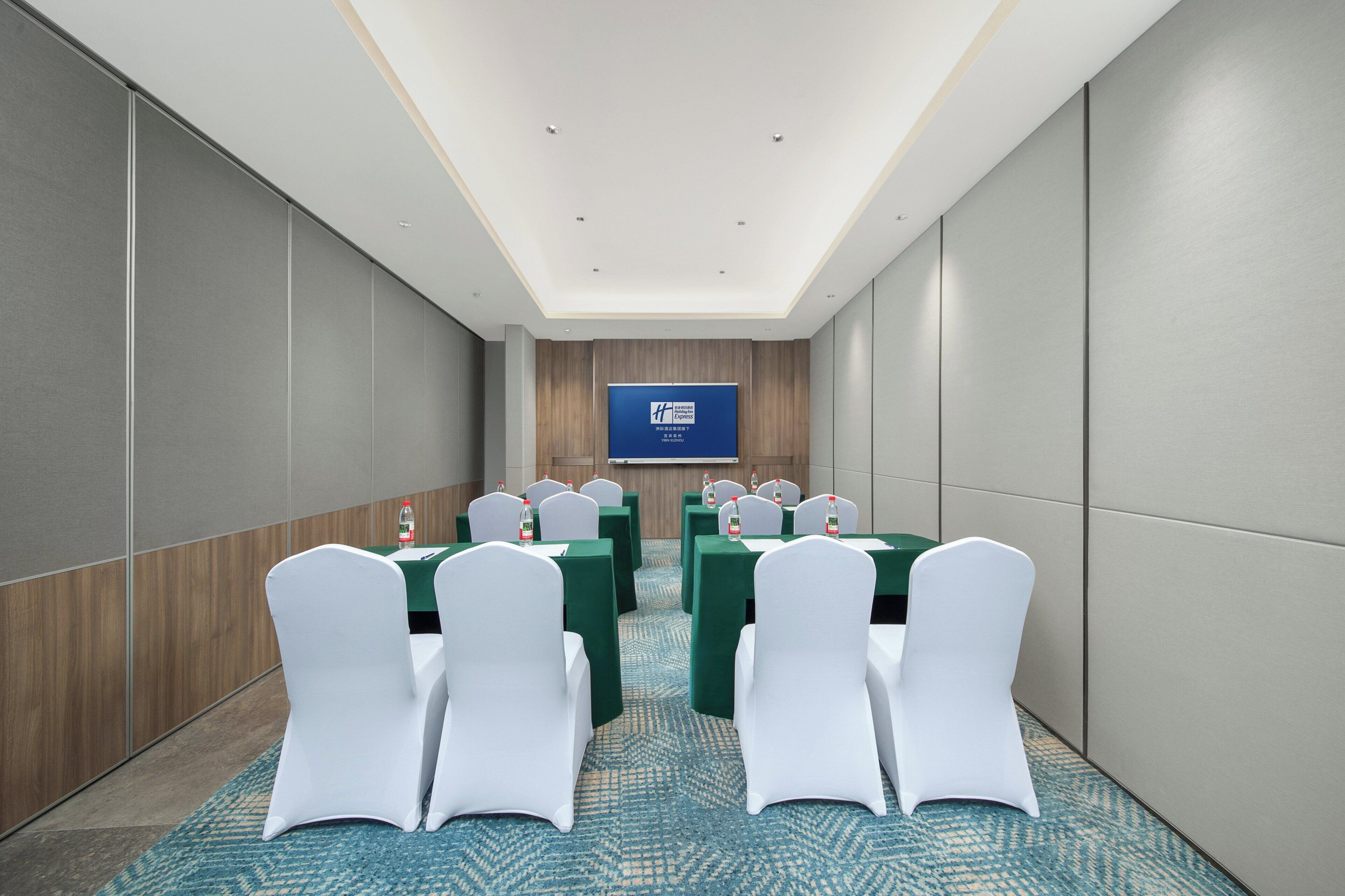 A conference room with a large screen, rows of tables, and white chairs.