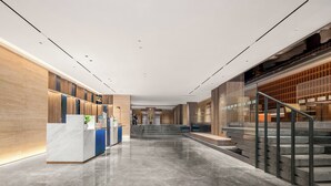 Eine moderne Hotelhalle mit Marmorboden, einem Holzbüro und einer Treppe zu einer oberen Etage.
